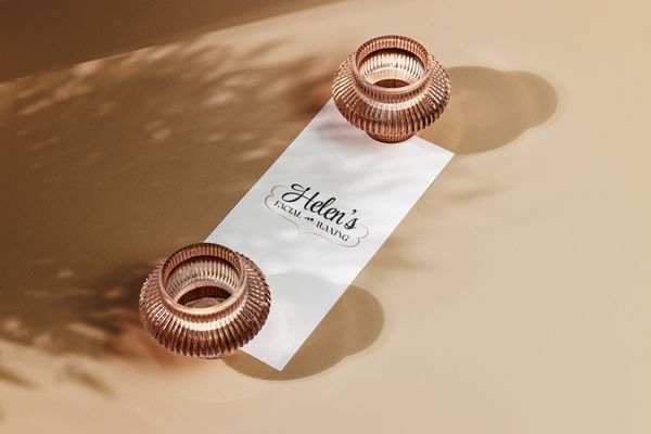 "Helen's Facial & Waxing" is written in cursive font on a white paper, set against a tan background with two bronze vases at each end of the paper.